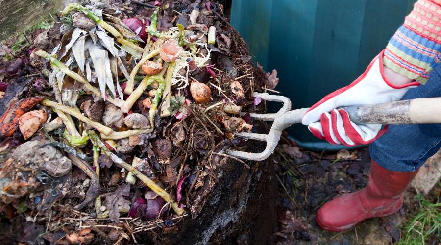 Photographie montrant une personne qui brasse et aère son compost afin de faire son compostage chez soi.