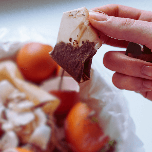 Photographie en gros plan d'une personne ajoutant un sachet de thé à son compost et qui permet d'illustrer le sujet de l'article suivant : Peut-on ajouter les sachets de thé à son compost ?